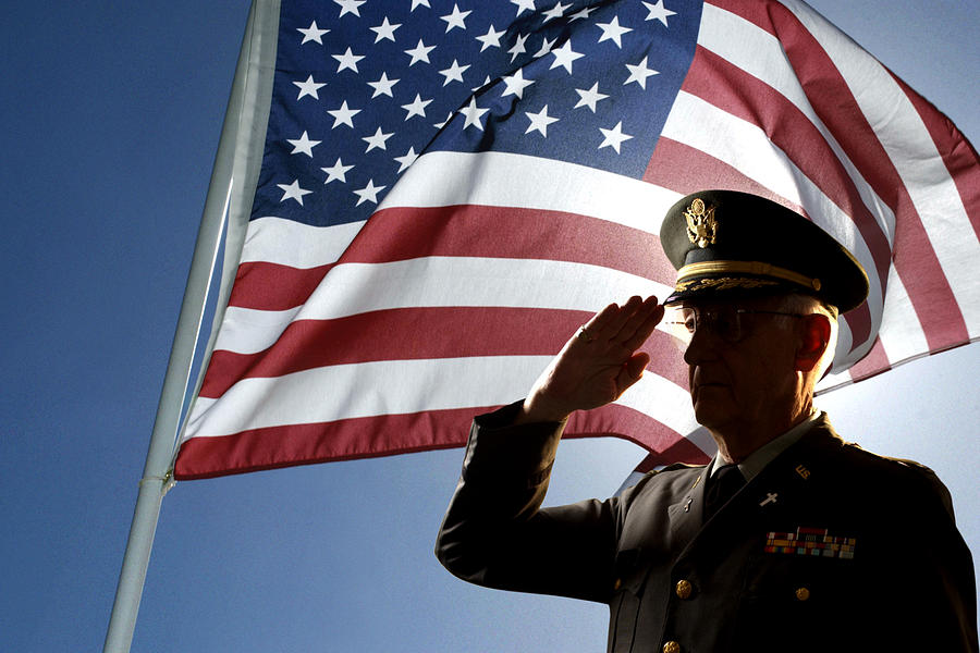 Silhouette of veteran US Army Colonel Chaplain wearing hat and saluting with an American flag flying behind him. Photograph by Thinkstock