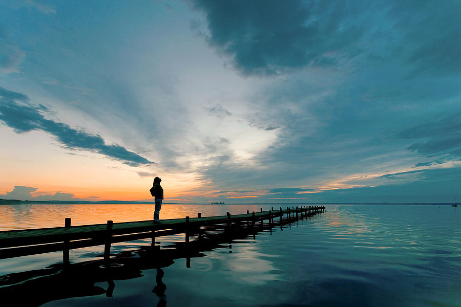 Silhouette of Woman on Lakeside Jetty with majestic Sunset Cloudscape Photograph by RelaxFoto.de