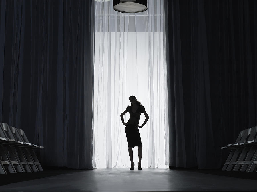 Silhouette of young woman standing on catwalk, hands on hips Photograph by Thomas Barwick