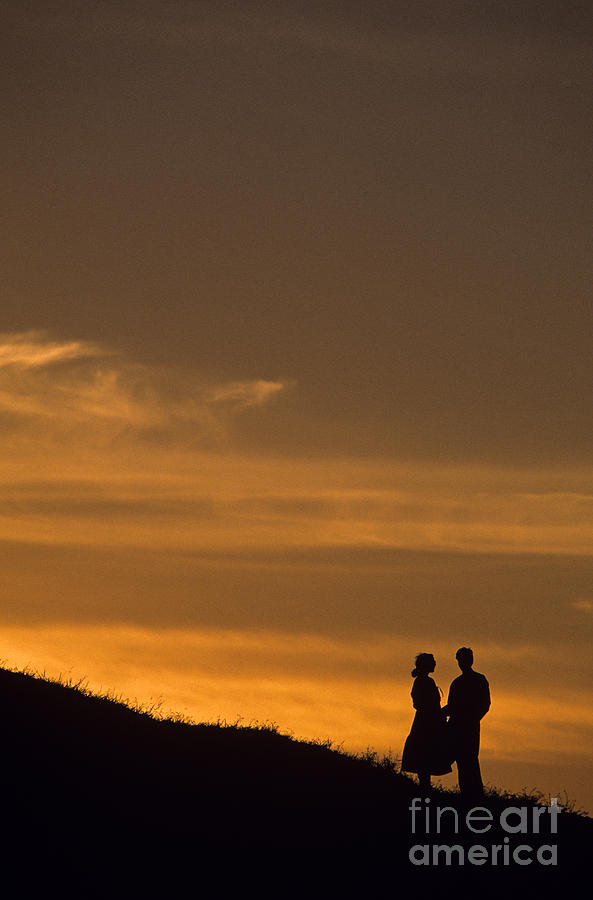 Silhouetted couple at sunset standing on bluff  Photograph by Jim Corwin