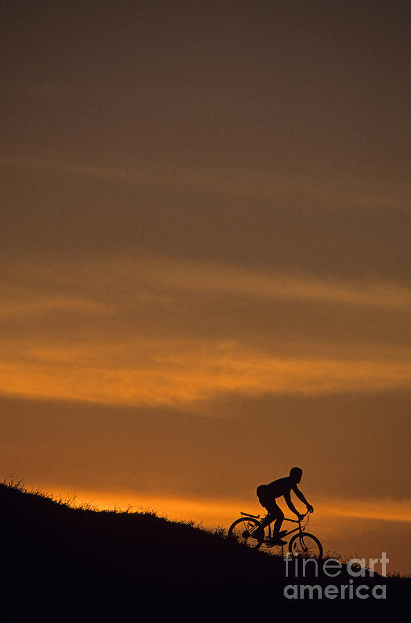 Silhouetted man on bicycle going down a hill at sunset Photograph by Jim Corwin