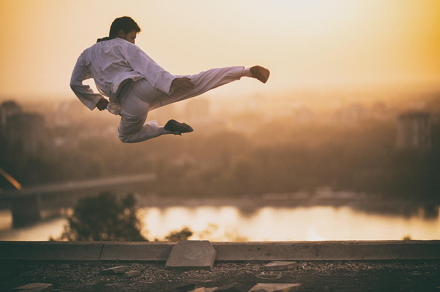 Skillful martial artist performing fly kick at sunset. Photograph by Skynesher