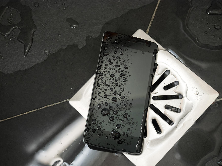 Smart mobile phone dropped on the floor of a shower next to the drain with water Photograph by Jose A. Bernat Bacete