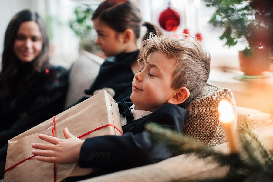 Smiling boy holding Christmas present while sitting with family in living room Photograph by Maskot