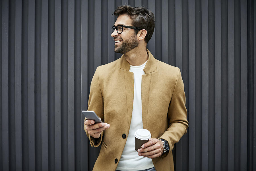 Smiling businessman with smart phone and cup Photograph by Morsa Images