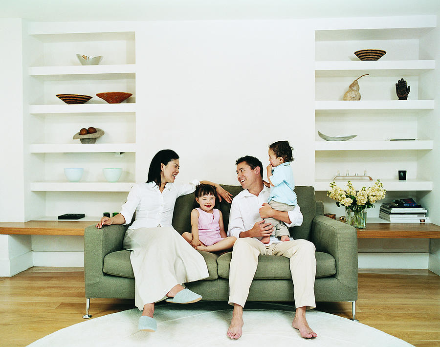 Smiling Family of Four Sitting on a Sofa in a Living Room Photograph by Digital Vision.