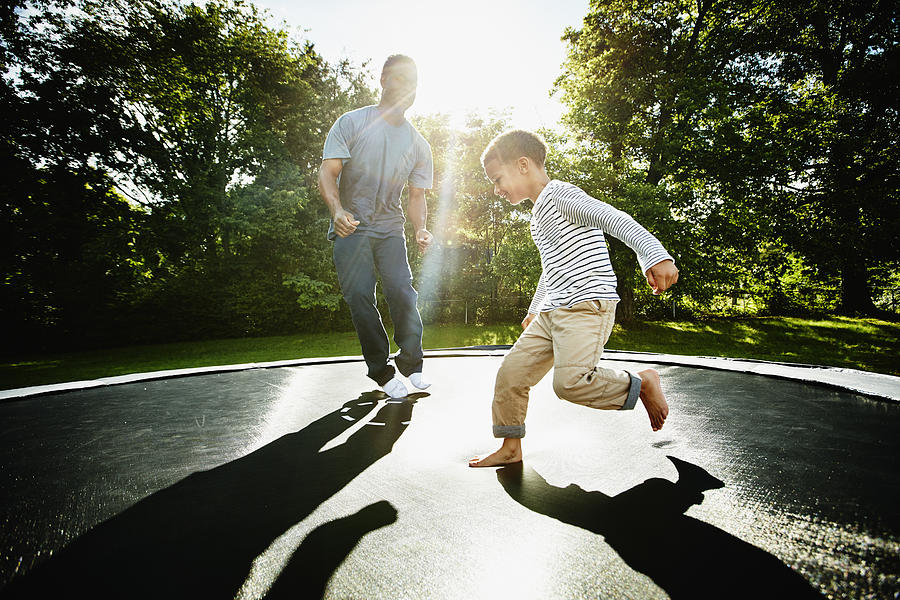 Smiling father and young son jumping on trampoline Photograph by Thomas Barwick
