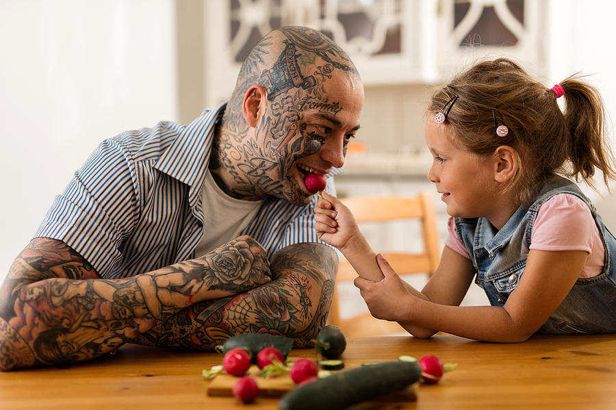 Smiling little girl feeding her father with a radish. Photograph by Skynesher
