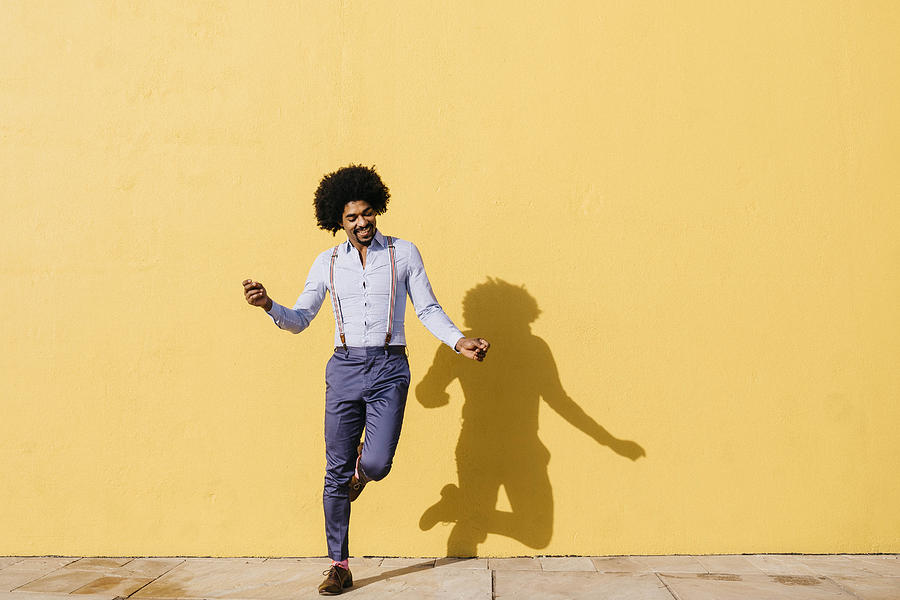 Smiling man dancing in front of yellow wall Photograph by Westend61