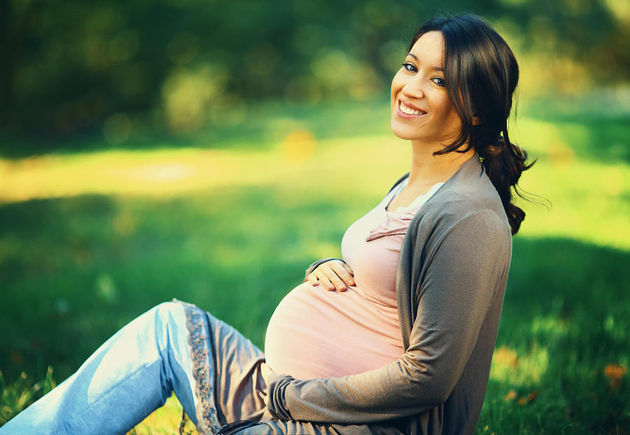 Smiling pregnant woman in a park. Photograph by Gilaxia