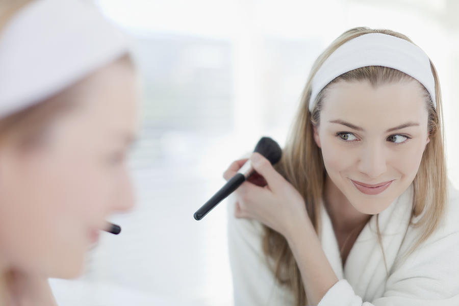 Smiling woman applying makeup Photograph by Hybrid Images