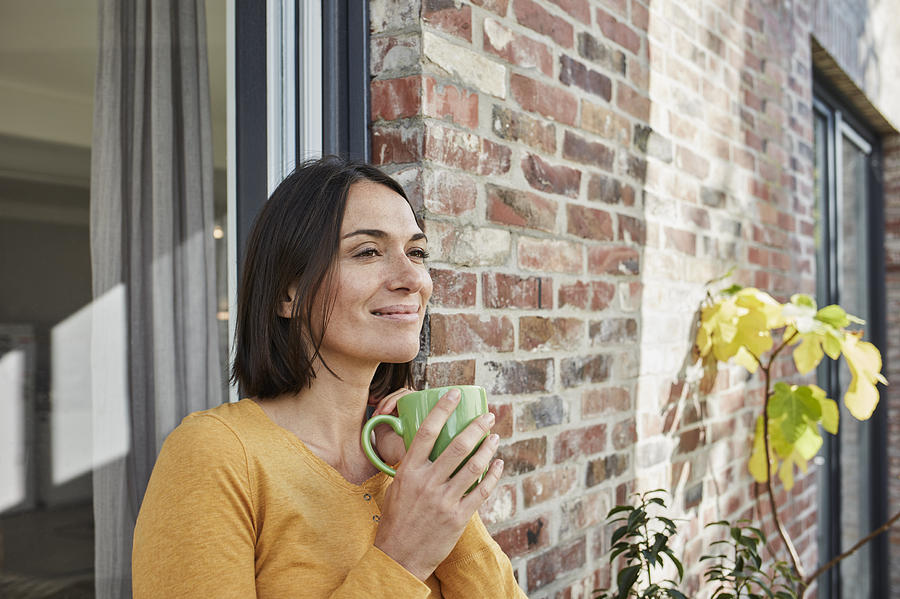 Smiling woman drinking from cup in front of her home Photograph by Westend61