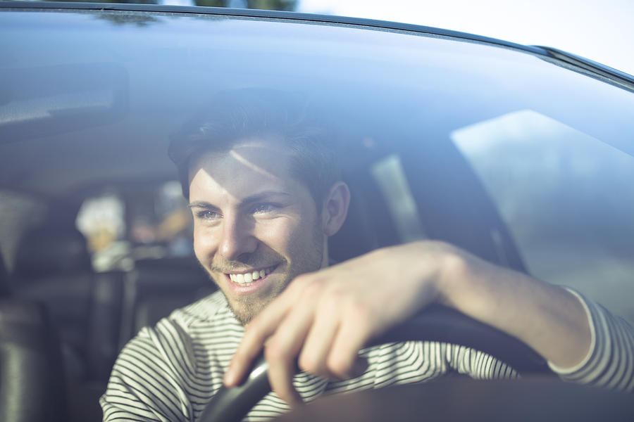 Smiling young man driving car Photograph by Westend61