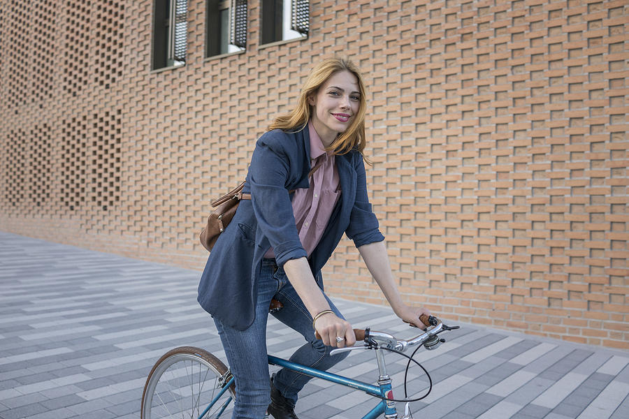 Smiling young woman riding bicycle in the city Photograph by Simon Ritzmann