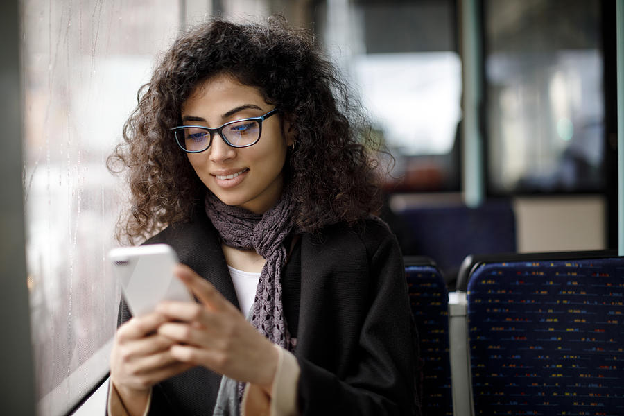 Smiling young woman traveling by bus and using smart phone Photograph by Damircudic