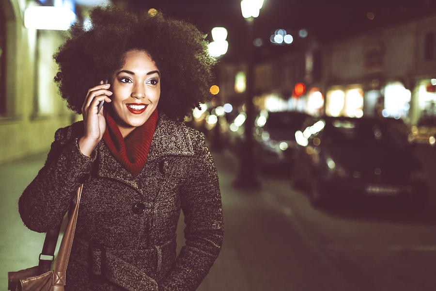 Smiling young woman using phone on street by night Photograph by Portishead1