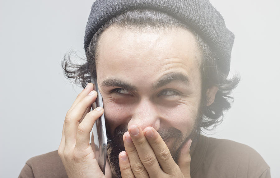Smirking young man talking on phone over gray background Photograph by Ismailciydem
