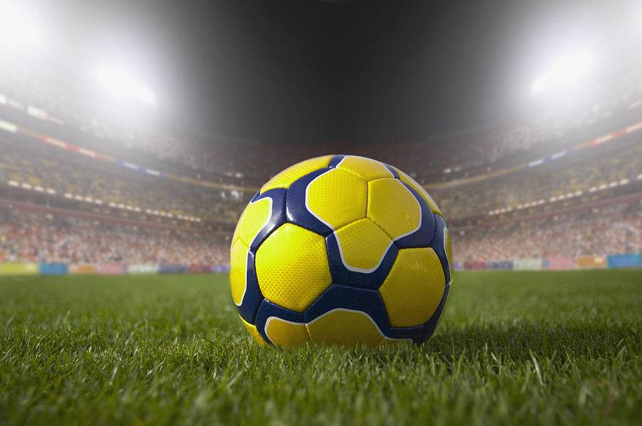 Soccer ball resting on grass in large stadium Photograph by Jon Feingersh Photography Inc