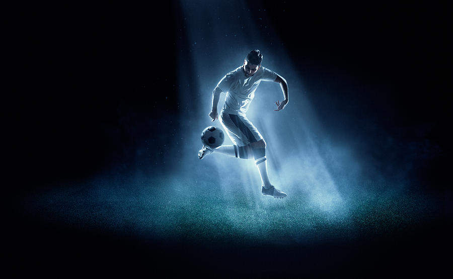 Soccer player kicking ball in spotlight Photograph by Dmytro Aksonov