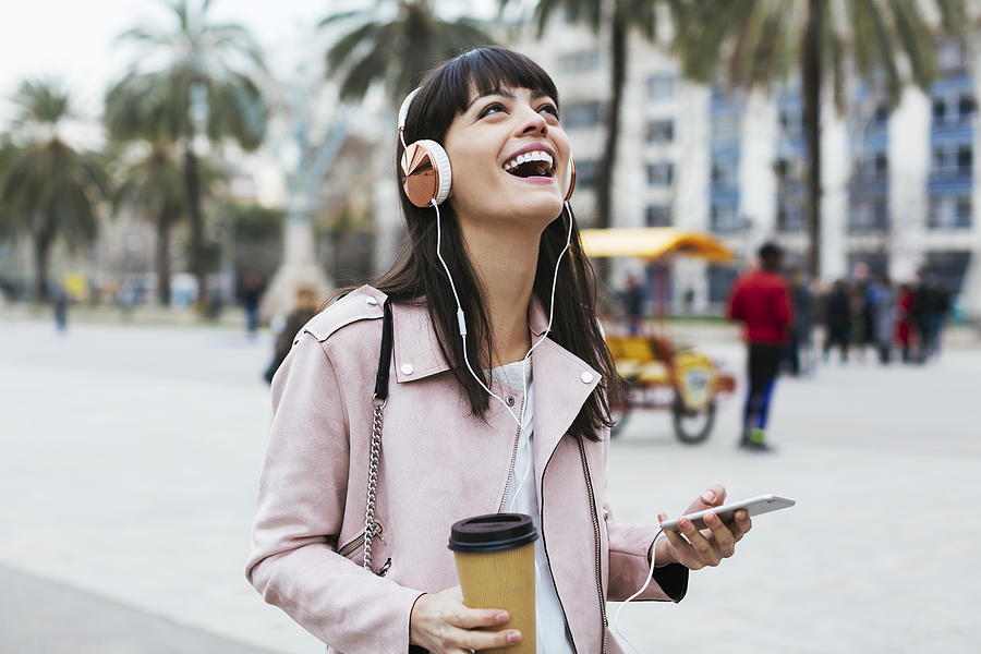 Spain, Barcelona, laughing woman with coffee, cell phone and headphones in the city Photograph by Westend61