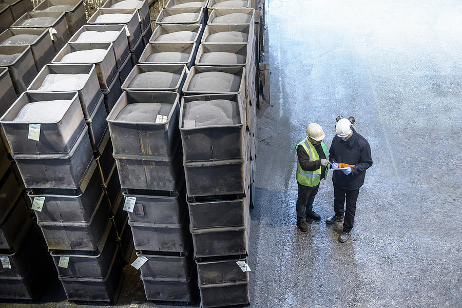 Steel workers in industrial steel foundry inspecting paperwork next to crates of steel shot, high angle view Photograph by Monty Rakusen