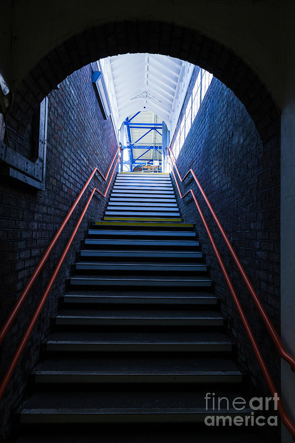 Steps up leading from dark to light with red hand rail. Photograph by Peter Noyce