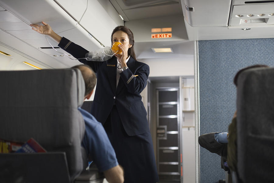 Stewardess explaining safety procedures to passengers on airplane Photograph by Jupiterimages