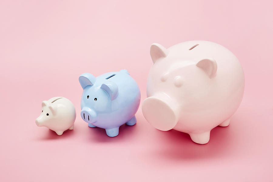 Still life of differently sized white, blue and pink piggy banks in ascending size order on pink background Photograph by The_burtons