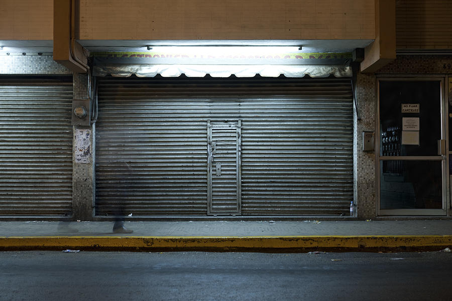Store front with locked roll-up door at night Photograph by PhotoAlto/Sandro Di Carlo Darsa