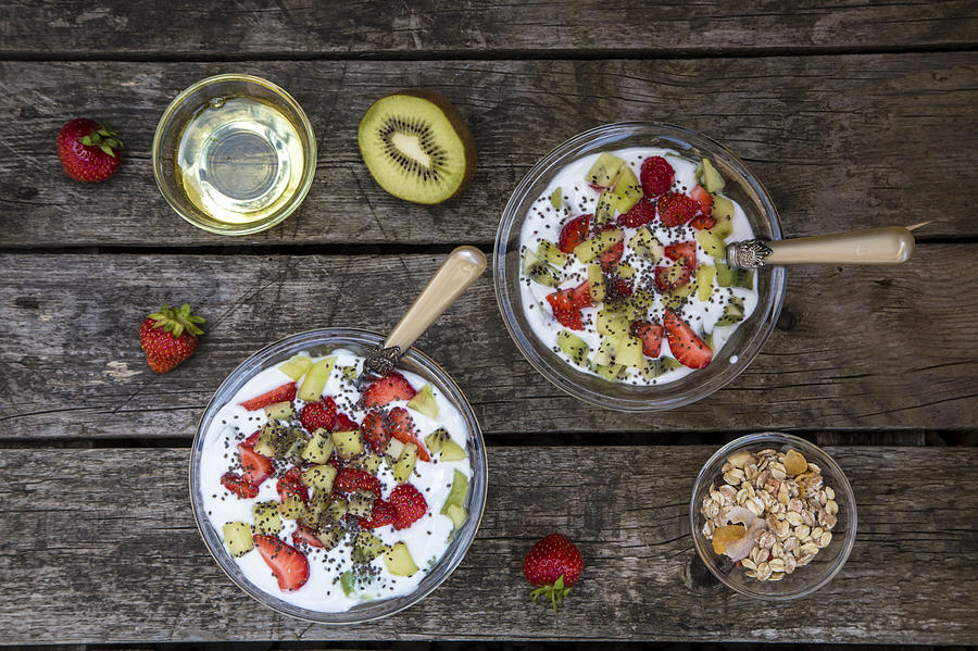 Strawberry kiwi yogurt with cereals, chia seeds, agave syrup in glass bowl on wood Photograph by Westend61