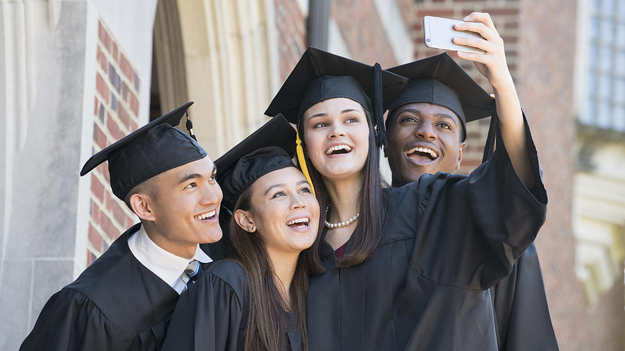 Students posing for cell phone selfie at graduation Photograph by Ariel Skelley