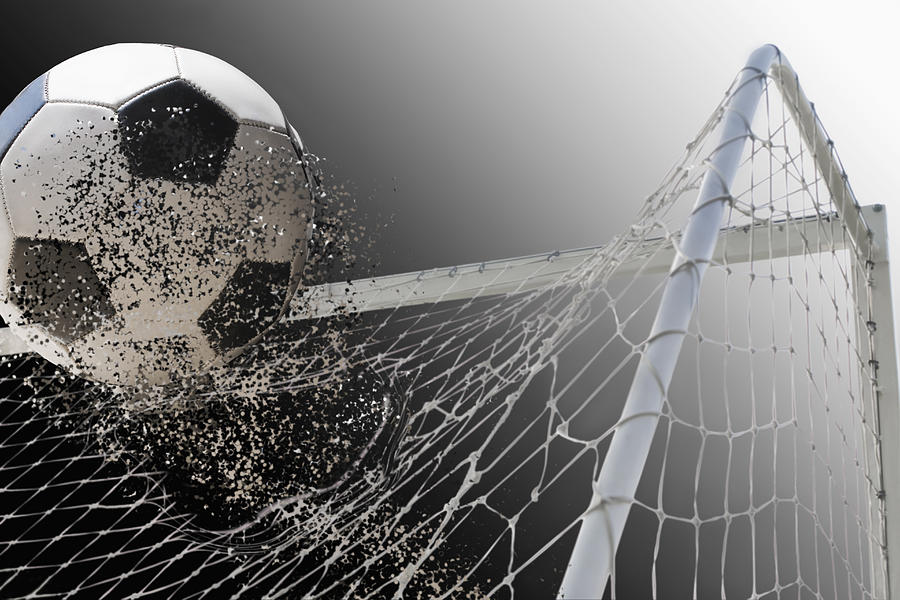 Studio shot of football powering through goal netting Photograph by REB Images