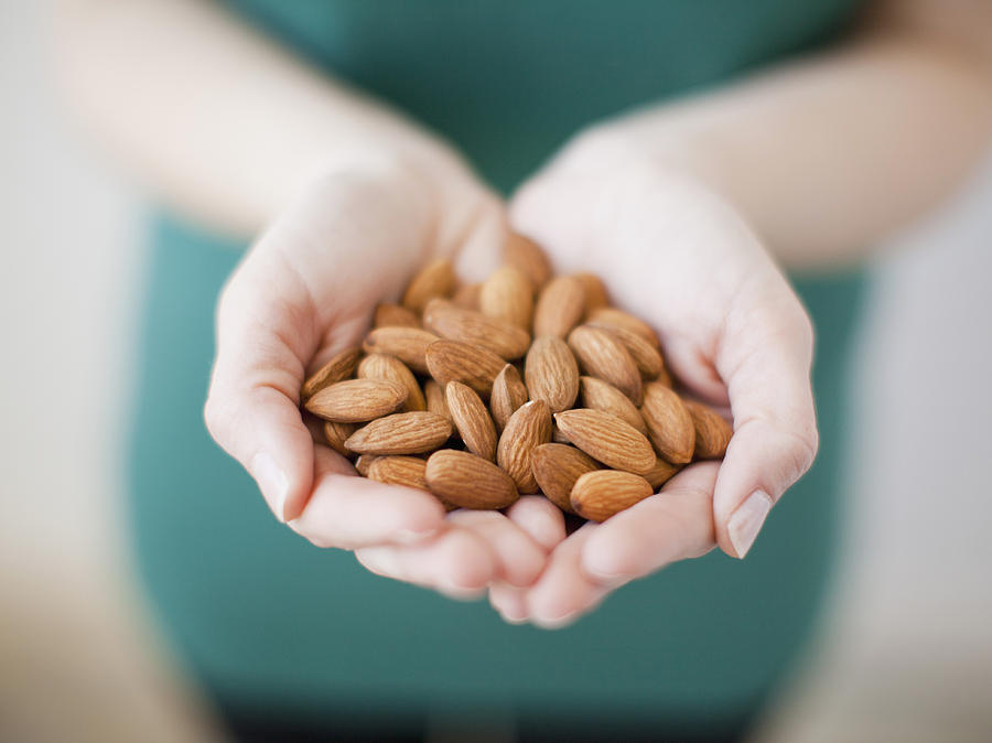 Studio shot of woman showing handful of almonds Photograph by Jessica Peterson