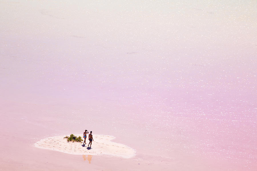 Stunning small island in the middle of the pink lagoon with couple enjoying the beach day in the Fuerteventura island during travel vacations. Photograph by Artur Debat