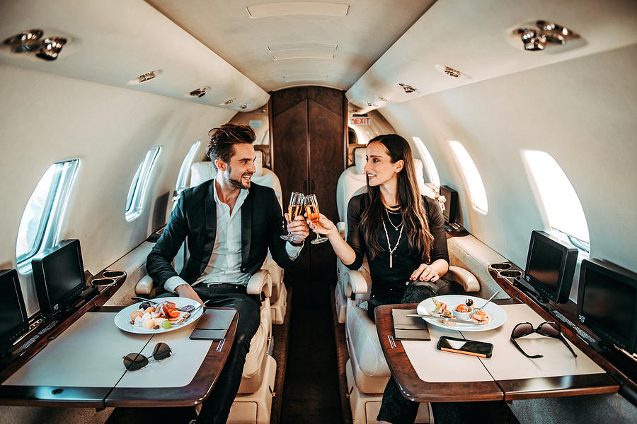 Successful couple making a toast with champagne glasses while having canapes aboard a private airplane Photograph by Extreme-photographer