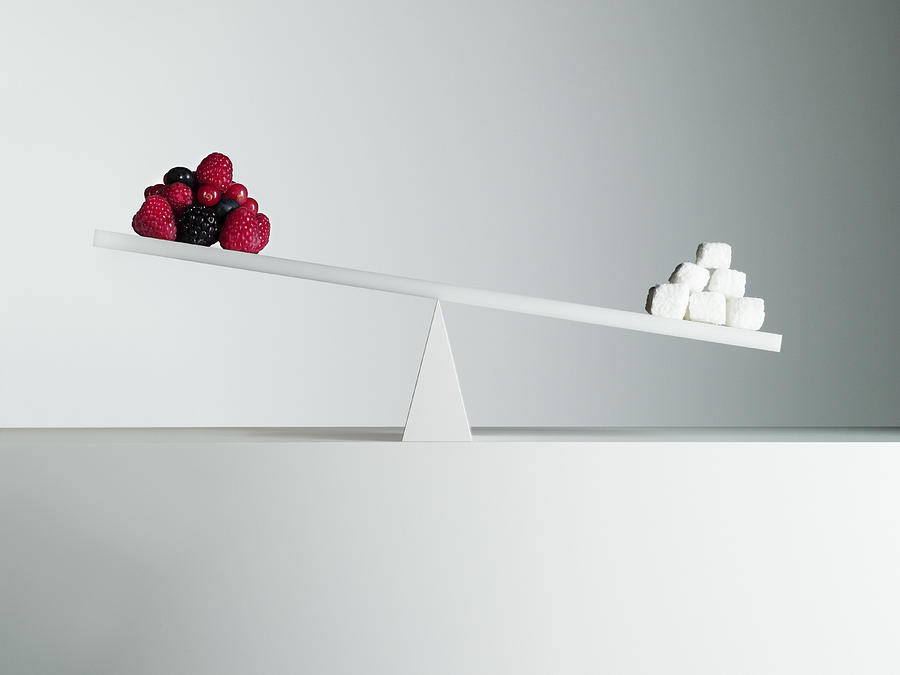 Sugar cubes tipping seesaw with berries on opposite end Photograph by Martin Barraud