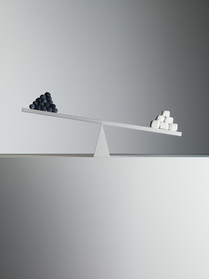 Sugar cubes tipping seesaw with blueberries on opposite end Photograph by Martin Barraud