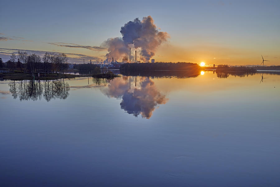Sunset on the Oulujoki River with blue sky, smokestacks and smoke clouds reflected in the water, Oulu, Finland Photograph by Andrew Merry