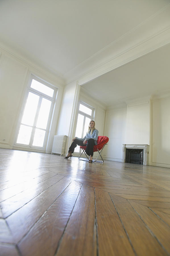 Surface Level Shot of a Woman Sitting on a Red Chair in a Large Empty Room with a Wooden Floor Photograph by B2M Productions