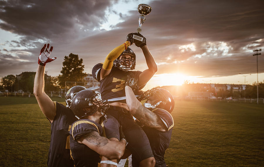Team of American football players celebrating victory at sunset. Photograph by Skynesher
