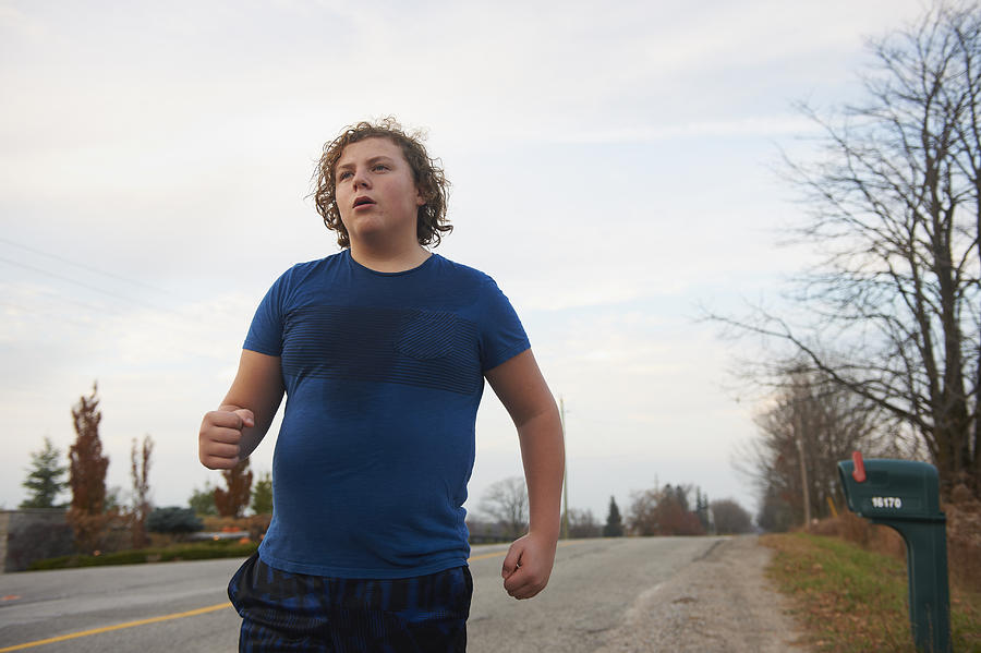 Teen boy jogging on country road Photograph by Lwa