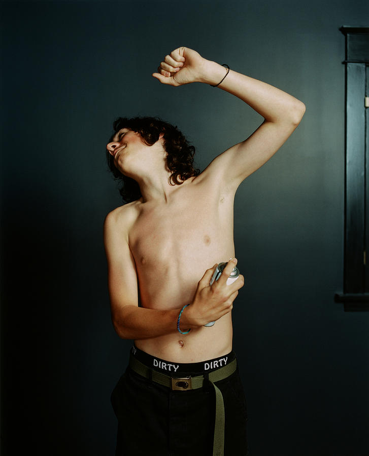 Teenage boy (14-16) spraying underarm with deodorant Photograph by Catherine Ledner