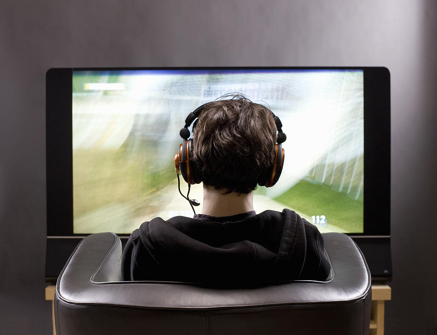 Teenage boy sits in front of TV playing video game Photograph by Schedivy Pictures Inc.