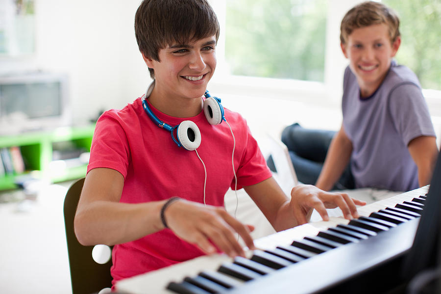 Teenage boy watching friend play electronic piano keyboard Photograph by Paul Bradbury