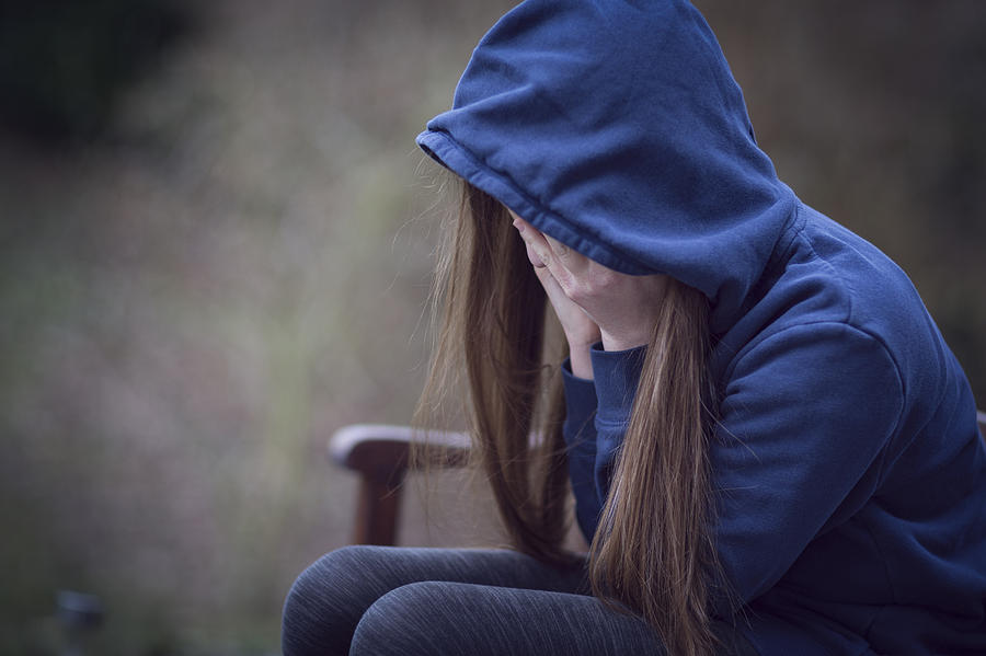 Teenage girl in hooded top, with head in hands in despair Photograph by Elva Etienne