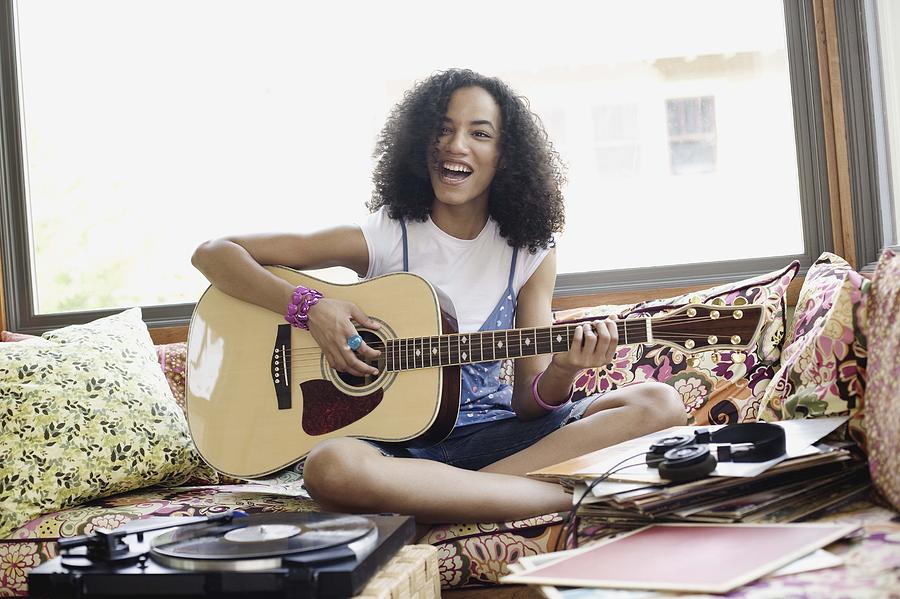 Teenage girl playing acoustic guitar and singing indoors Photograph by Jupiterimages