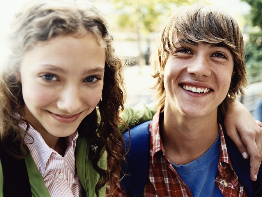Teenage Girl Stands Smiling With Her Arm Around Her Friend Photograph by Digital Vision.