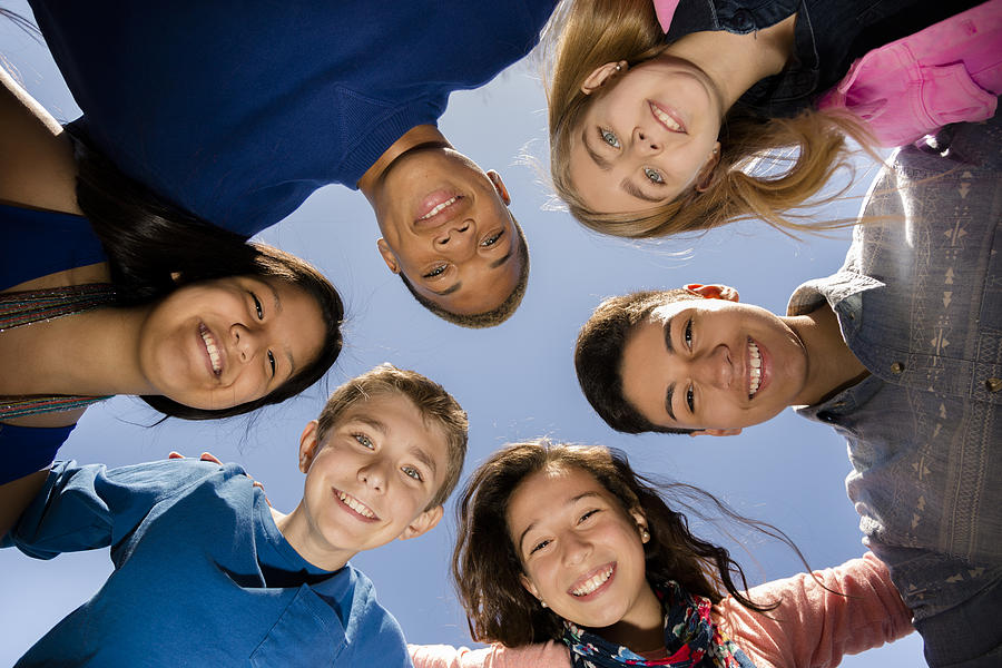 Teenagers: Diverse group of friends huddle outside together. Blue sky. Photograph by Fstop123