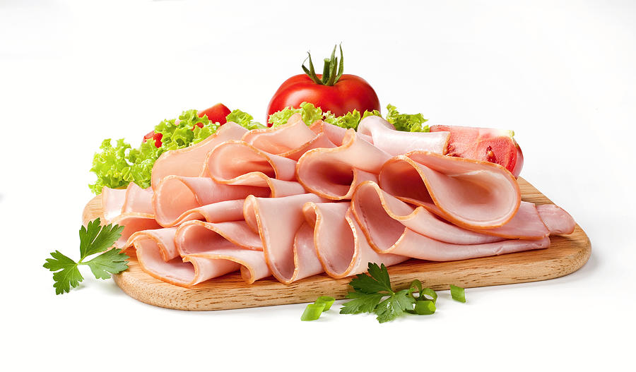 Thinly sliced ham and veggies atop a wooden cutting board Photograph by Milanfoto