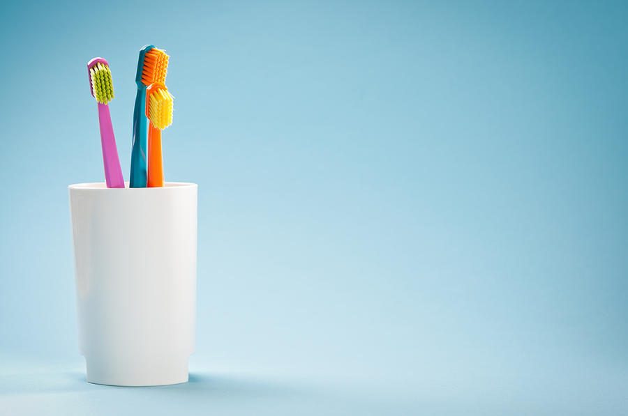 Three colourful soft toothbrushes in white mug on blue background Photograph by Domin_domin